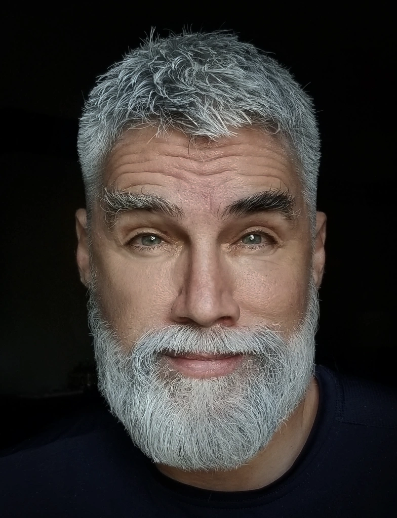 Short, textured silver hair with a full beard; suitable for casual and formal occasions, exuding a polished look.