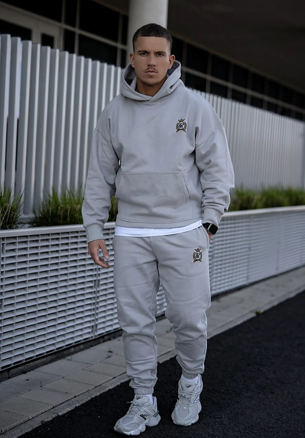 Man poses outside in a pale grey hoodie and joggers, finished with chunky white sneakers and smartwatch.